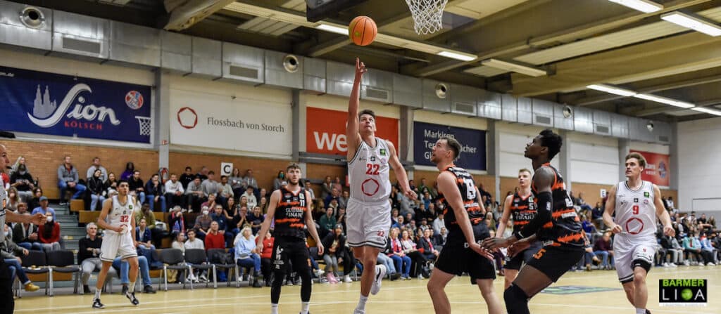 Basketballspiel der RheinStars Köln in weiß gegen Team in schwarz-orange; Spieler springt zum Wurf.