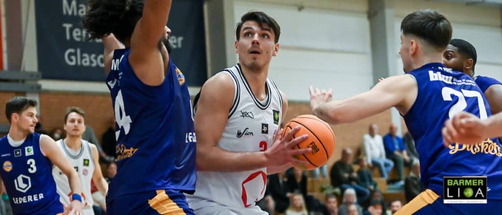 Basketballspiel: RheinStars-Spieler in Weiß dribbelt gegen blaue Verteidiger.