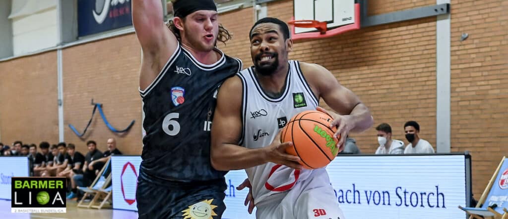 Basketballspiel der RheinStars Köln: Spieler in Weiß mit Ball gegen Gegner in Schwarz.