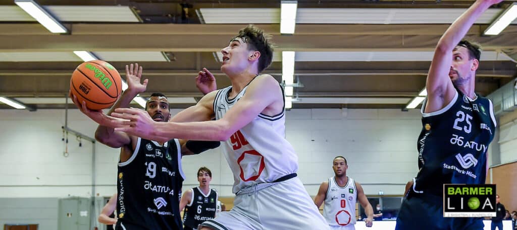Basketballspiel: Spieler in weißem Trikot mit Ball umgeben von Gegnern in dunklen Trikots.