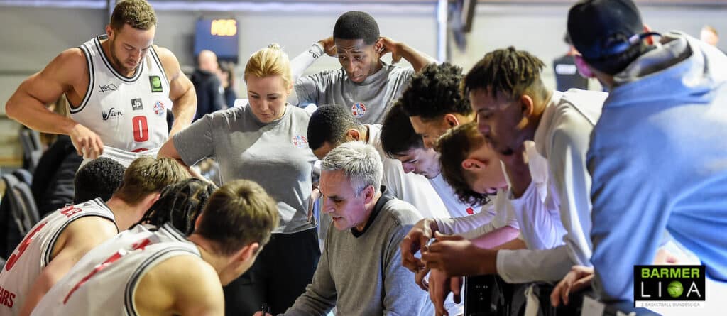 Trainerteam der RheinStars Köln gibt Anweisungen während einer Spielerpause in der Halle.