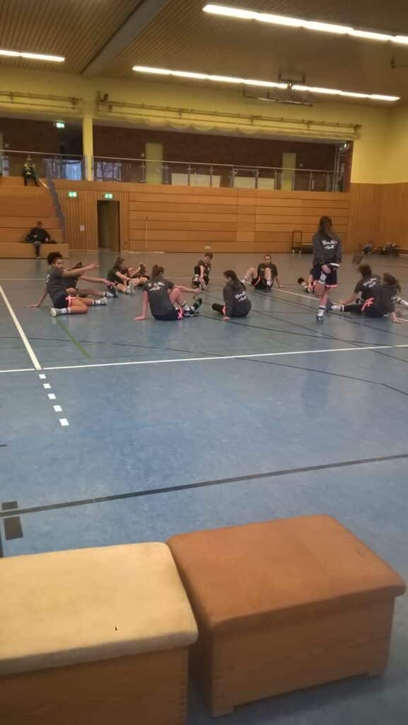 Trainingsgruppe der RheinStars Köln sitzt auf grauem Hallenboden während Übung.