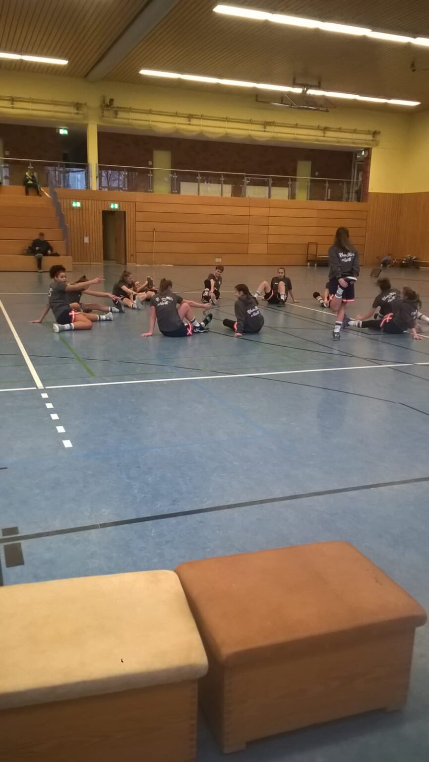 Trainingsgruppe der RheinStars Köln sitzt auf grauem Hallenboden während Übung.