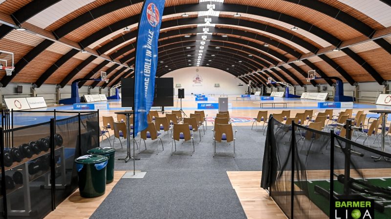 Sporthalle der RheinStars Köln mit Basketballplätzen, Zuschauerstühlen und gewölbter Holzdecke.