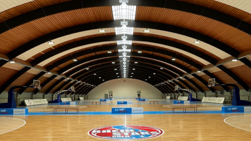 Sporthalle der RheinStars Köln mit Basketballplatz und gewölbter Holzdecke.