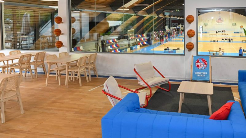 Lounge des Campus der RheinStars Köln mit Blick auf die Basketballhalle, Sitzmöbeln und Dekoration.