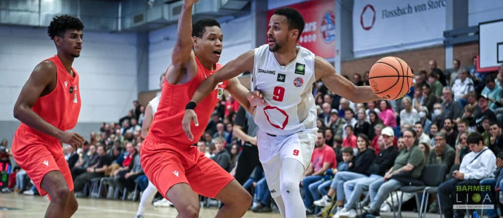 Basketballspiel der RheinStars Köln: Spieler in Weiß dribbbelt gegen zwei Gegenspieler in Rot.