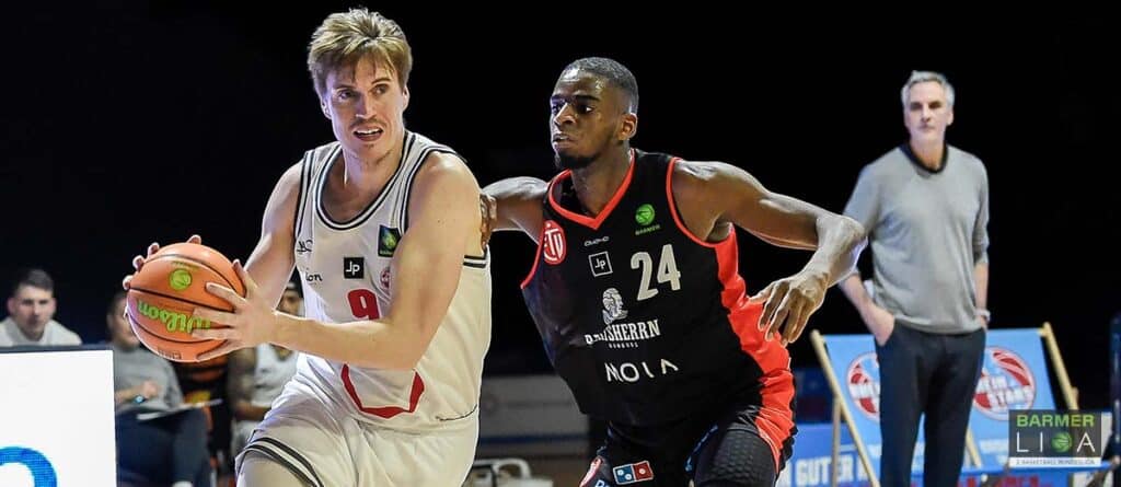 Basketballspiel: RheinStars-Spieler in Weiß dribbelt gegen Abwehrspieler in Schwarz-Rot.