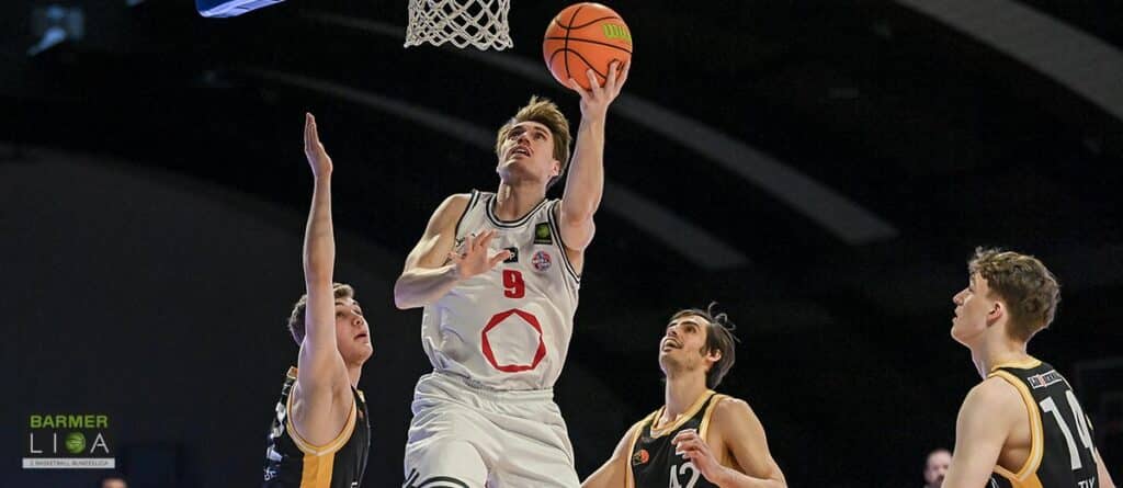Basketballspieler der RheinStars Köln wirft Ball während Ligaspiel gegen gegnerisches Team.