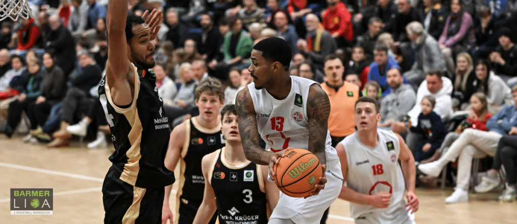 Basketballspiel der RheinStars Köln: Spieler in Weiß mit Ball gegen Gegner in Schwarz-Gold.