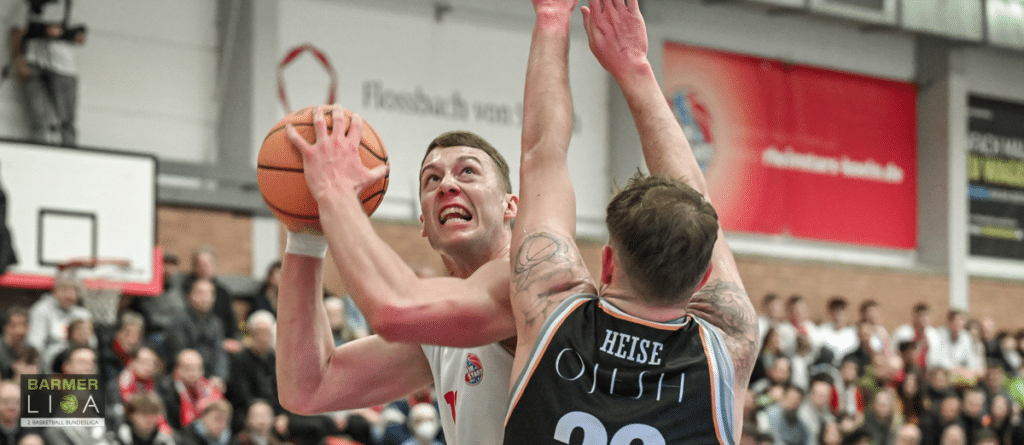Basketballspieler der RheinStars Köln wirft Ball unter Druck eines Gegenspielers.