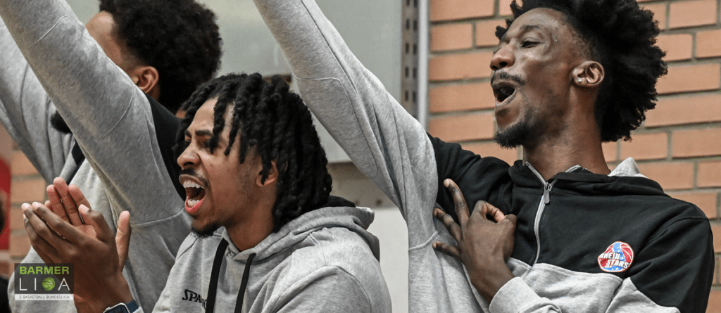 Drei Spieler der RheinStars Köln jubeln emotionsgeladen auf der Bank.