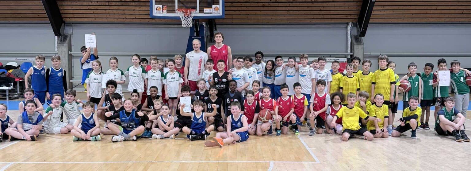 Große Gruppe von Kindern und Jugendlichen der RheinStars Köln in einer Sporthalle, posierend für ein Teamfoto.