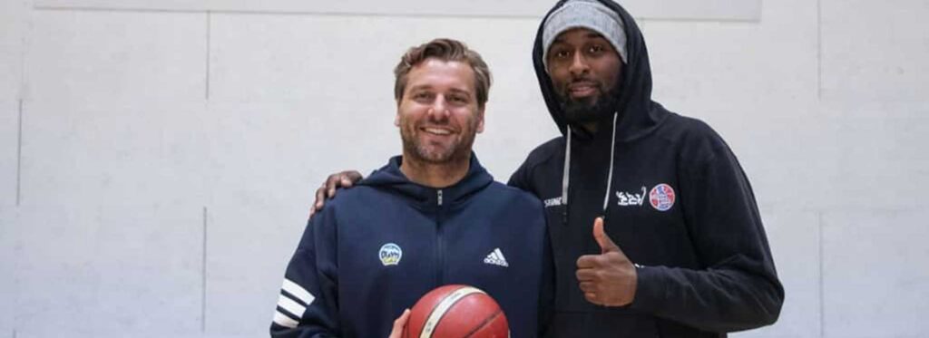 Zwei Männer posieren zusammen mit Basketball in einer Sporthalle der RheinStars Köln.