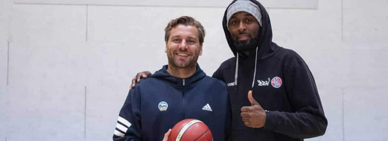 Zwei Männer posieren zusammen mit Basketball in einer Sporthalle der RheinStars Köln.