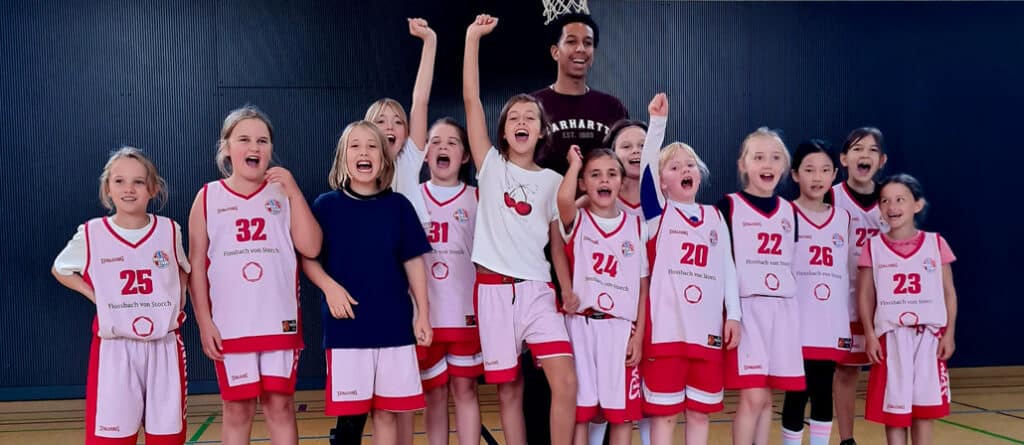 Mädchen-Basketballmannschaft der RheinStars Köln jubelt in Sportuniformen in einer Halle.