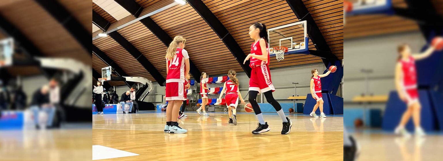 Junge Basketballspielerinnen der RheinStars Köln in roten Trikots während eines Spiels in einer Sporthalle.