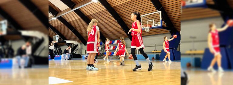 Junge Basketballspielerinnen der RheinStars Köln in roten Trikots während eines Spiels in einer Sporthalle.