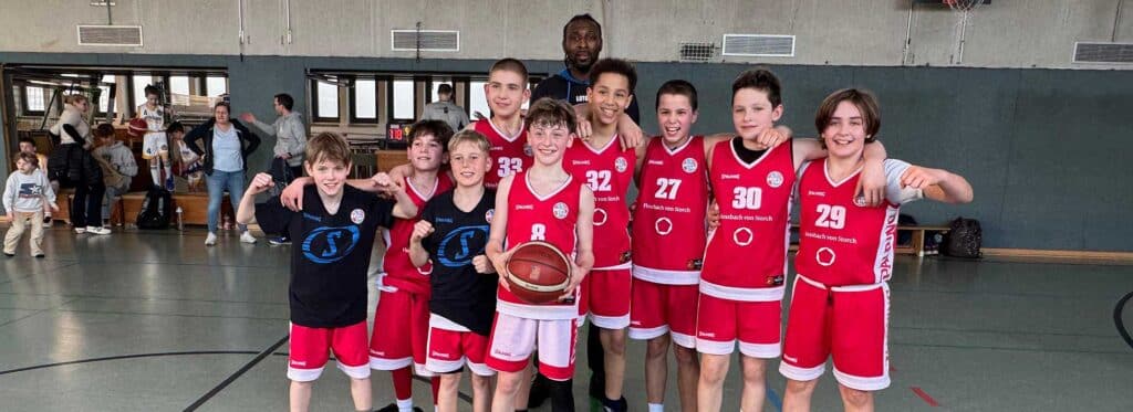Basketballmannschaft RheinStars Köln posiert mit Coach in der Sporthalle.