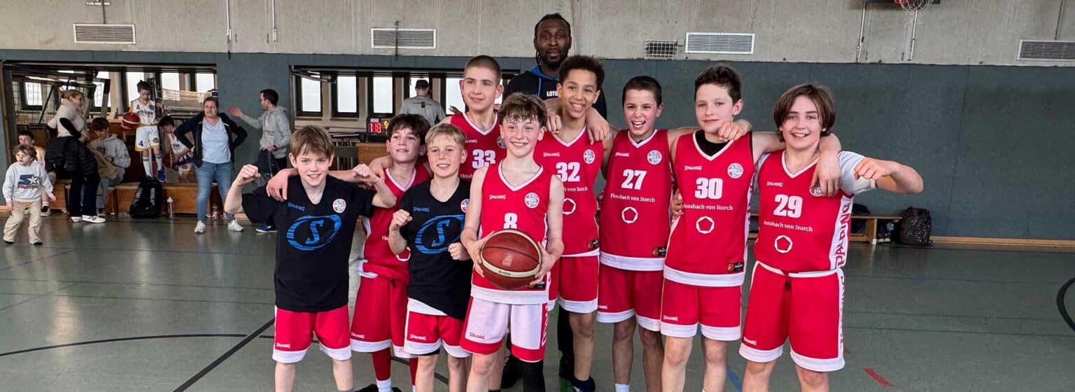 Basketballmannschaft RheinStars Köln posiert mit Coach in der Sporthalle.