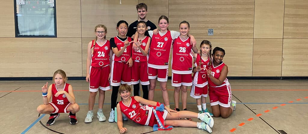 RheinStars Köln Basketballteam posiert in roter Uniform in einer Sporthalle.