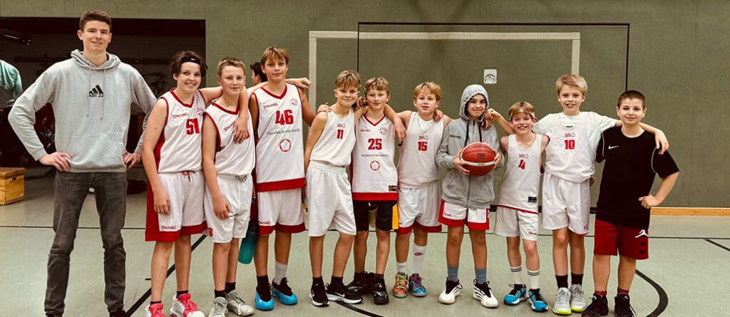 Basketballmannschaft RheinStars Köln posiert in Sporthalle mit Trainers und jungen Spielern in Trikots.