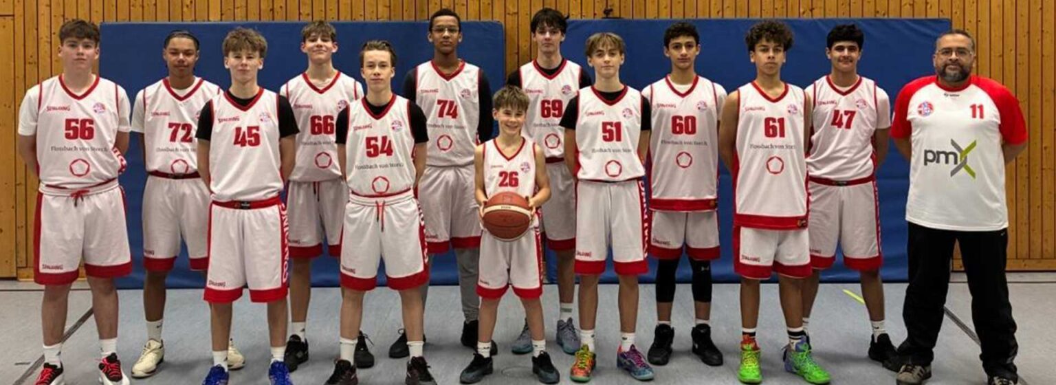 Mannschaftsfoto der RheinStars Köln Basketballteam in weiß-roten Trikots mit Trainer in einer Sporthalle.