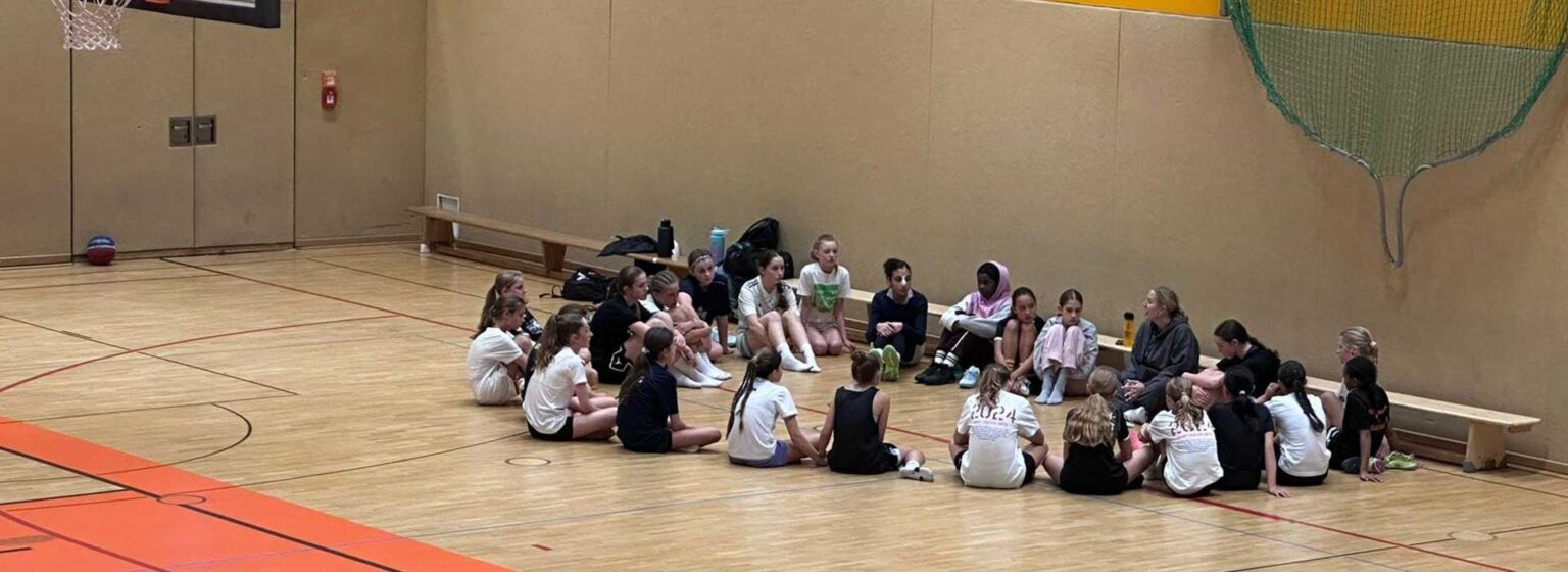 Gruppe von Kindern sitzt im Kreis auf dem Hallenboden der RheinStars Köln.