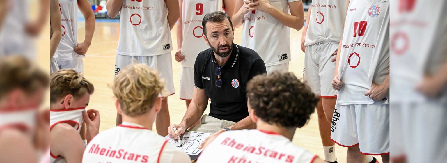 Trainer der RheinStars Köln erklärt Spielzug während Time-out vor versammelter Mannschaft.