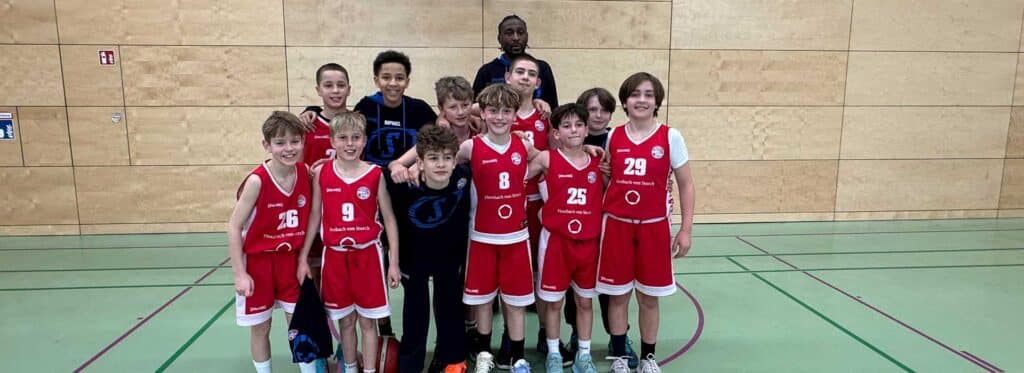 Jugendbasketballmannschaft RheinStars Köln in roten Trikots posiert in einer Sporthalle.