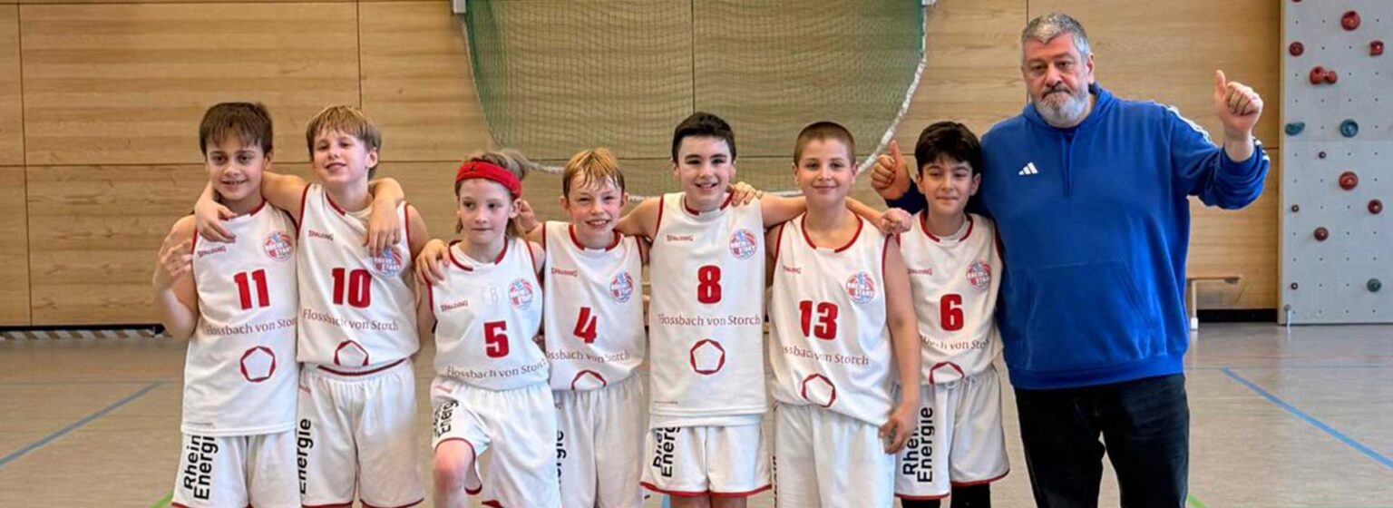Basketballmannschaft der RheinStars Köln mit Trainer in einer Sporthalle.