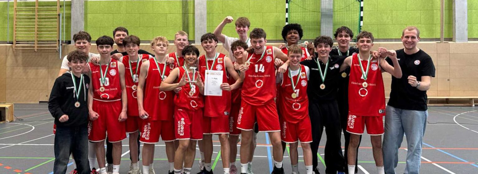 Basketballmannschaft RheinStars Köln mit Medaillen in Sporthalle, Trainer und Spieler posieren zusammen.