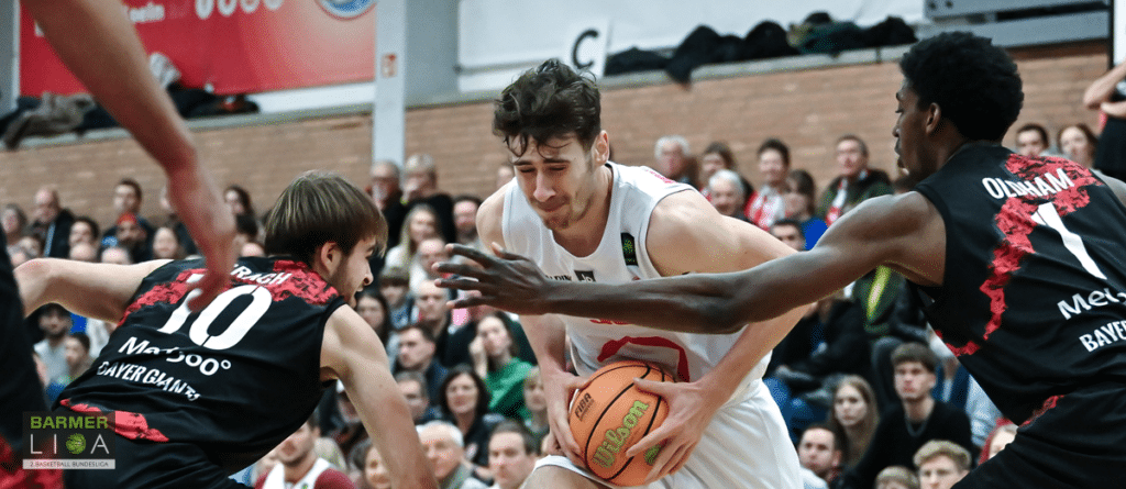 Basketballspiel der RheinStars Köln: Spieler im weißen Trikot dribbled gegen Gegner in schwarzem Trikot mit roten Mustern.