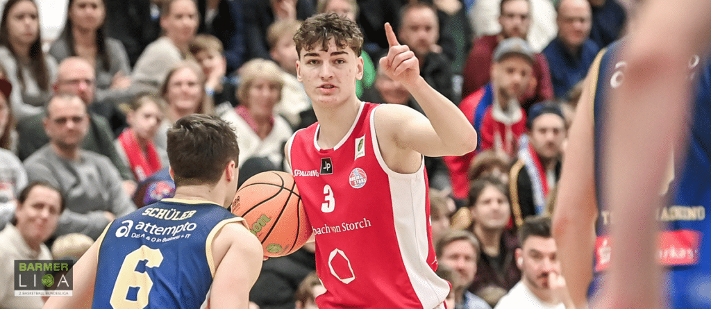 Basketballspieler der RheinStars Köln in rotem Trikot mit Nummer 3 zeigt während eines Spiels gestikulierend auf seinen Gegenspieler.