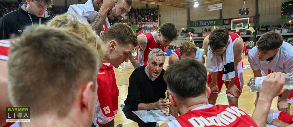 Trainer bespricht mit RheinStars-Köln-Basketballern Spielzüge auf Tablet während Timeout.
