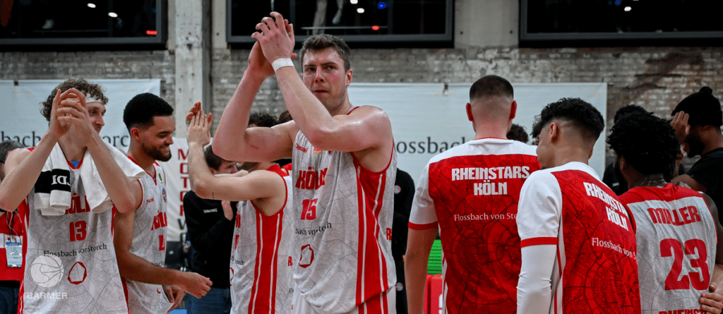 Basketballmannschaft RheinStars Köln feiert Sieg mit Teamgeste in der Halle.