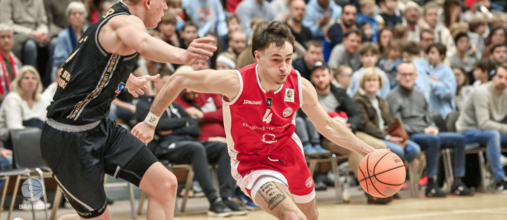 RheinStars-Spieler in rotem Trikot dribbelt Basketball gegen Gegner in schwarzem Trikot.