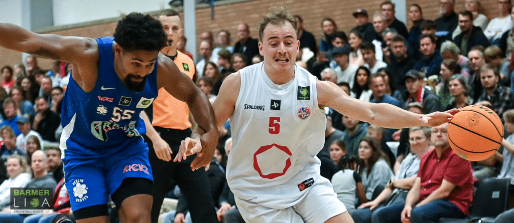 Basketballspiel der RheinStars Köln: Spieler in Weiß mit Nummer 5 dribbelt gegen Gegner in Blau.
