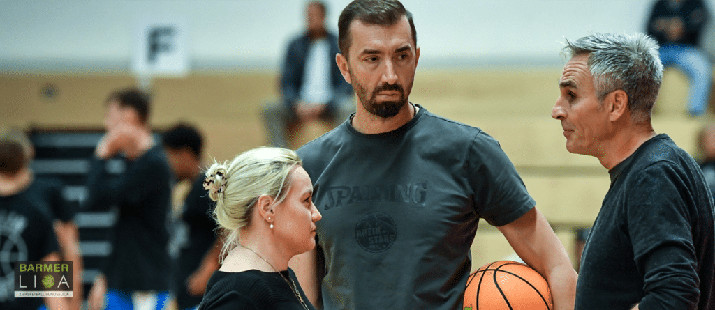 Drei Personen in einer Sporthalle diskutieren mit einem Basketball in der Hand.