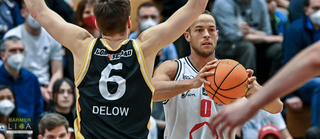 Basketballspiel: Spieler in weißem Trikot mit Ball gegen Gegner in schwarzem Trikot Nummer 6.