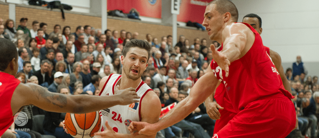 Basketballspiel der RheinStars Köln: Spieler in rot und weiß kämpfen um den Ball vor Publikum in der Halle.