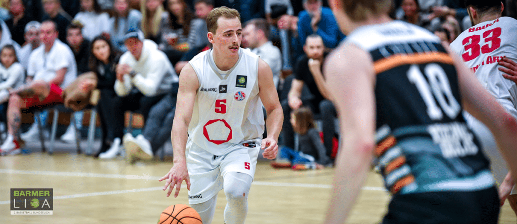 Basketballspieler der RheinStars Köln in weißem Trikot mit Nummer 5 dribbelt während eines Spiels.