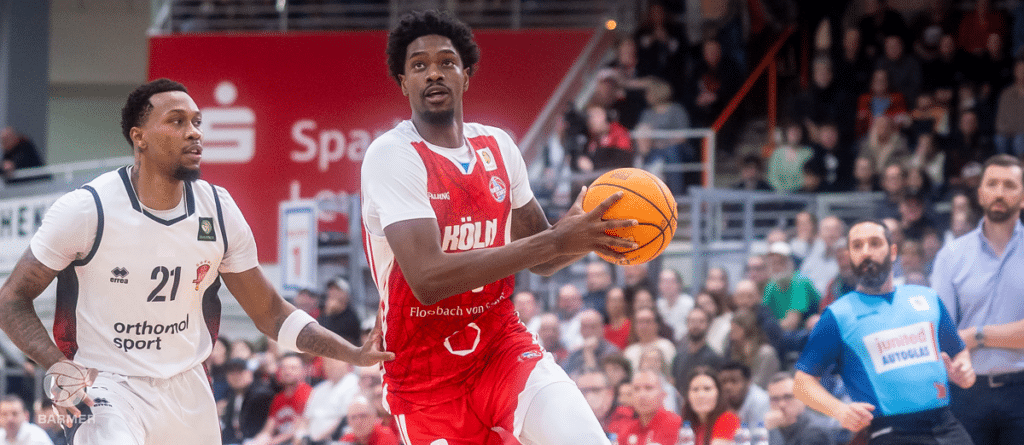 Basketballspieler der RheinStars Köln in rotem Trikot dribbelt gegen Gegner in weißem Trikot.
