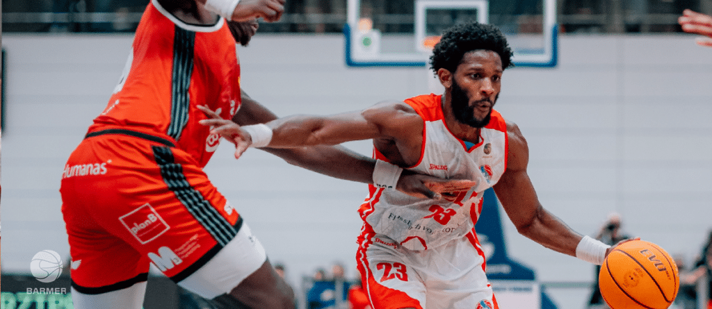 Basketballspieler der RheinStars Köln dribelt gegen Gegner in rotem Trikot.