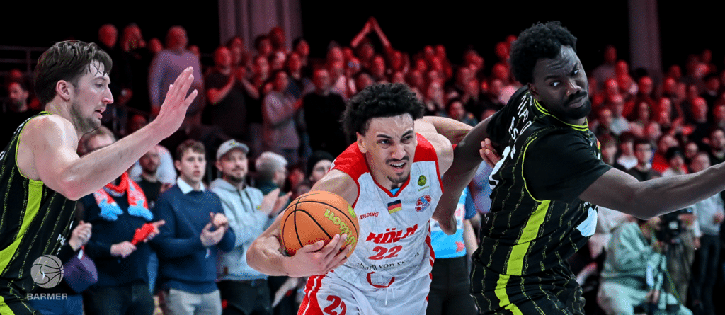 Basketballspiel der RheinStars Köln: Spieler in rotem Trikot dribbelt zwischen Gegnern in neongelb-schwarzen Uniformen.