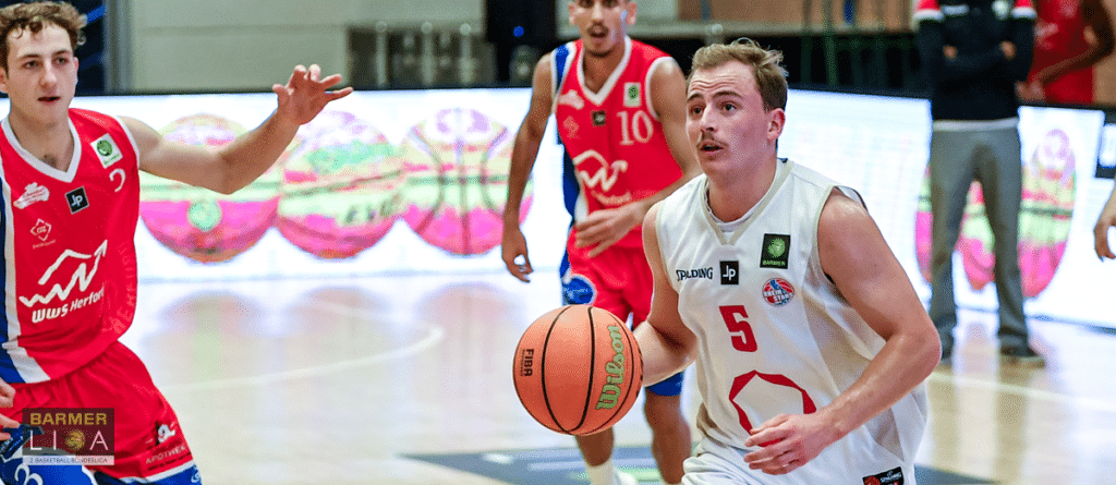 Basketballspieler der RheinStars Köln in weißem Trikot dribbert gegen rote Gegner.