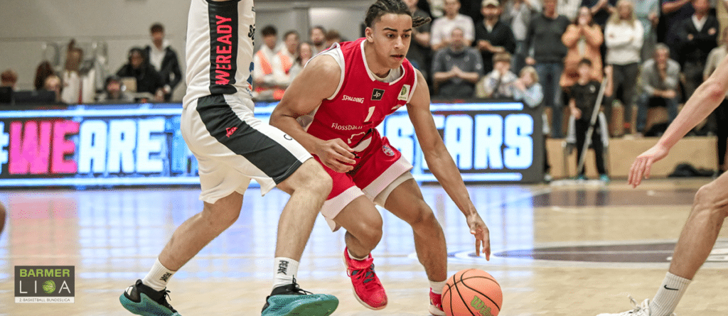 Basketballspieler der RheinStars Köln dribbelt in rotem Trikot gegen Verteidiger in weiß-schwarzer Kleidung.