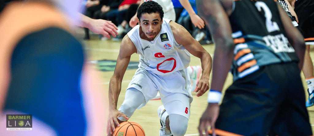 Basketballspieler der RheinStars Köln dribbelt den Ball in weißem Trikot während eines Spiels.