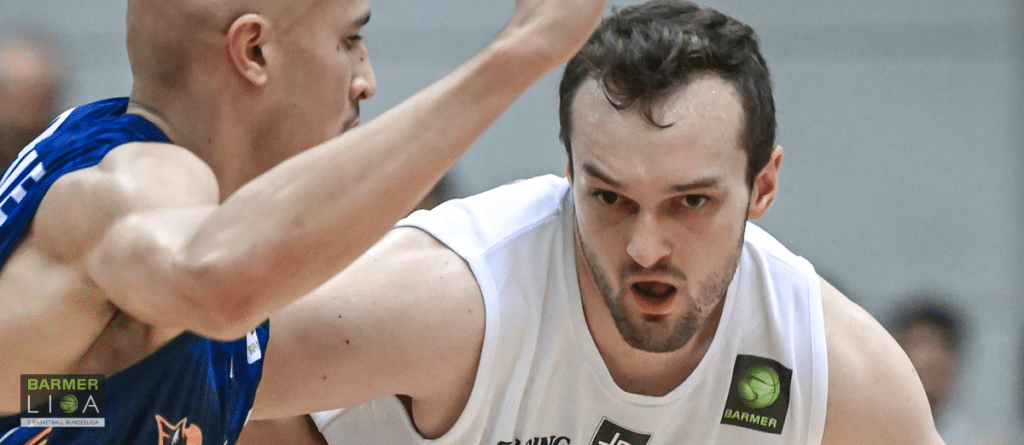 Basketballspieler der RheinStars Köln im weißen Trikot dribbelt gegen Gegner im blauen Trikot.