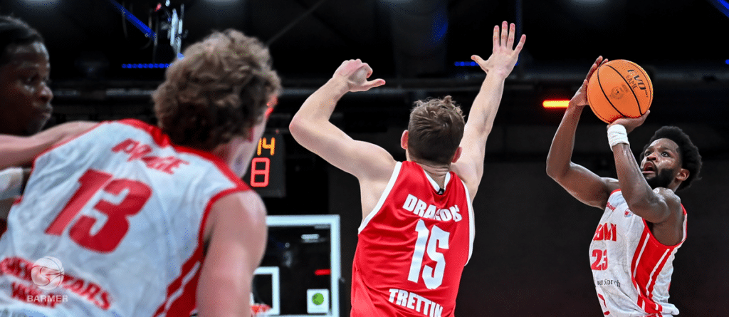 Basketballspieler der RheinStars Köln beim Wurf gegen Abwehrspieler in rotem Dress.